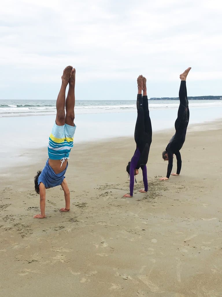 Three people doing hand stands on a beach